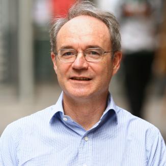 a man in a blue shirt and glasses, with grey hair